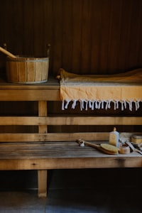 A wooden sauna bench with a bucket, yellow towel, and bath accessories