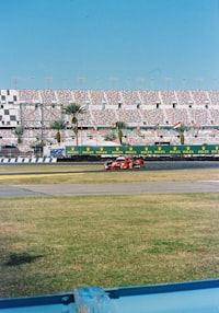 A red race car driving on a track in front of large stadium seating