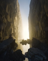A person on a rock ledge in a narrow canyon with glowing light