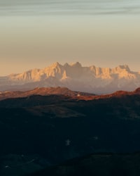 Jagged mountain peaks glowing in golden light above dark forested hills