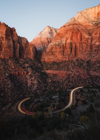 Light trails from a vehicle winding along a road through Zion National Park at golden hour